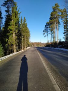 Aurinkoinen katumaisema, jossa näkyy kuvanottajan varjo.
